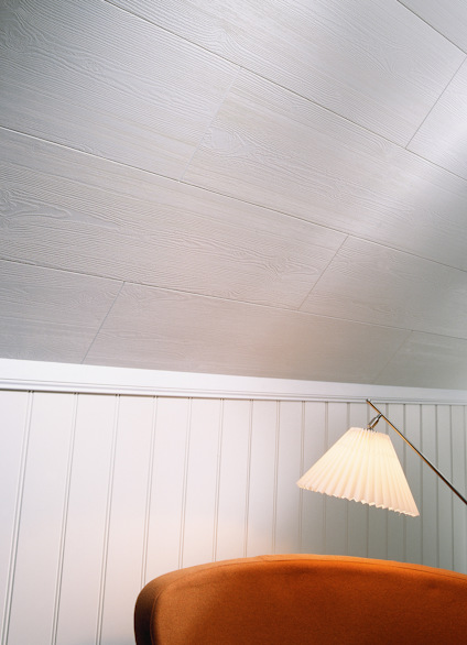 Vitt träpaneltak och vägg med vita lodräta paneler; en golvlampa med vit skärm vid en brun soffa.