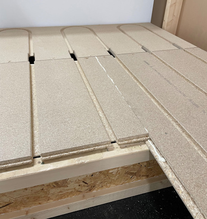 Plywoodskivor med frästa spår, delvis installerade på en träställning.