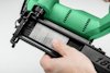 Person laddar en grön spikpistol med en rad metallspikar i en svart magasin.