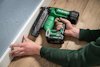 Person som håller en grön HiKOKI spikpistol mot en vit list mot en blå vägg.